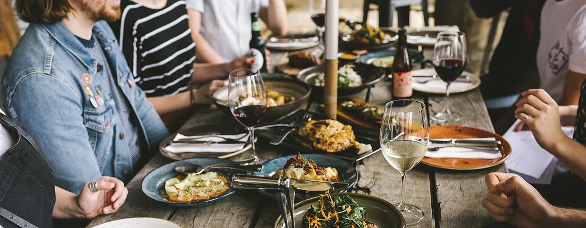 Friends around a long wooden table with wine and shared plates